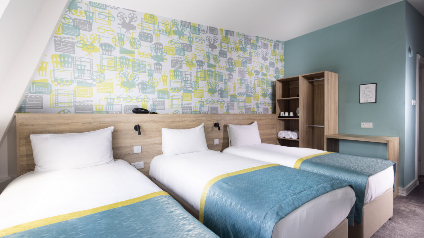 Modern hotel room with three cosy single beds, vibrant decor, ample storage, and a welcoming atmosphere for families.