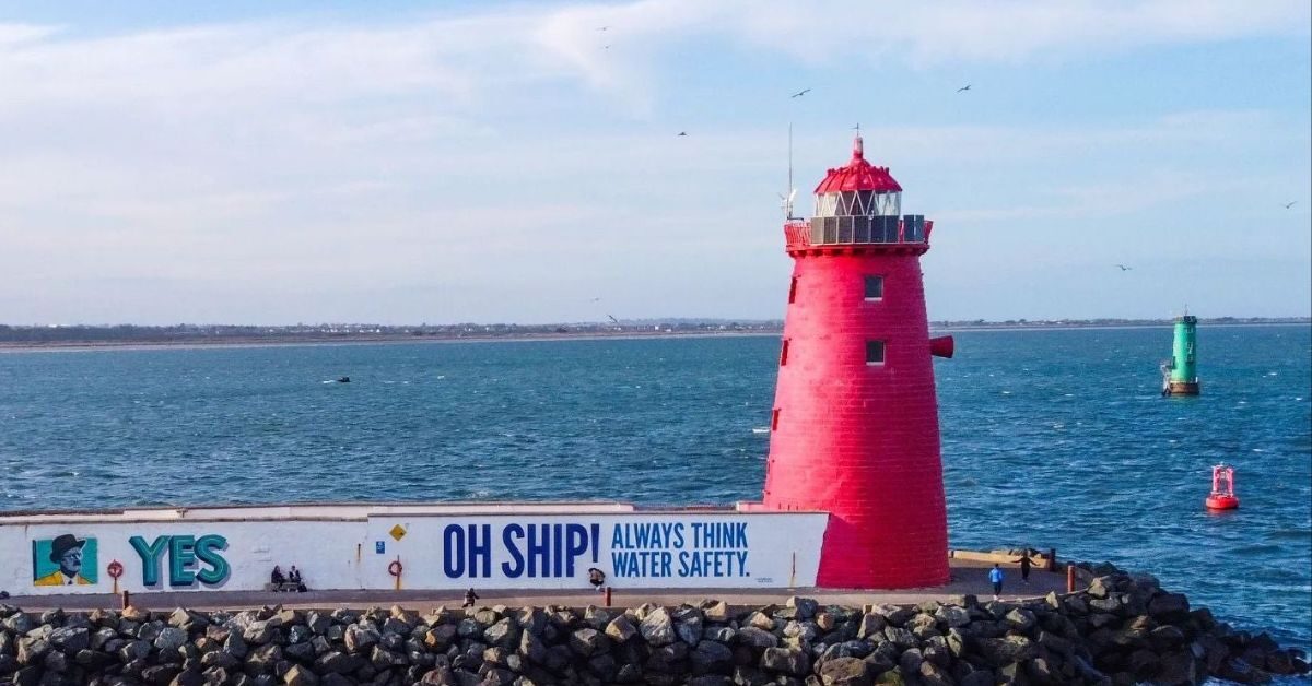 Iconic red lighthouse overlooking calm sea, perfect for seaside strolls. Vibrant mural adds charm to coastal retreat.